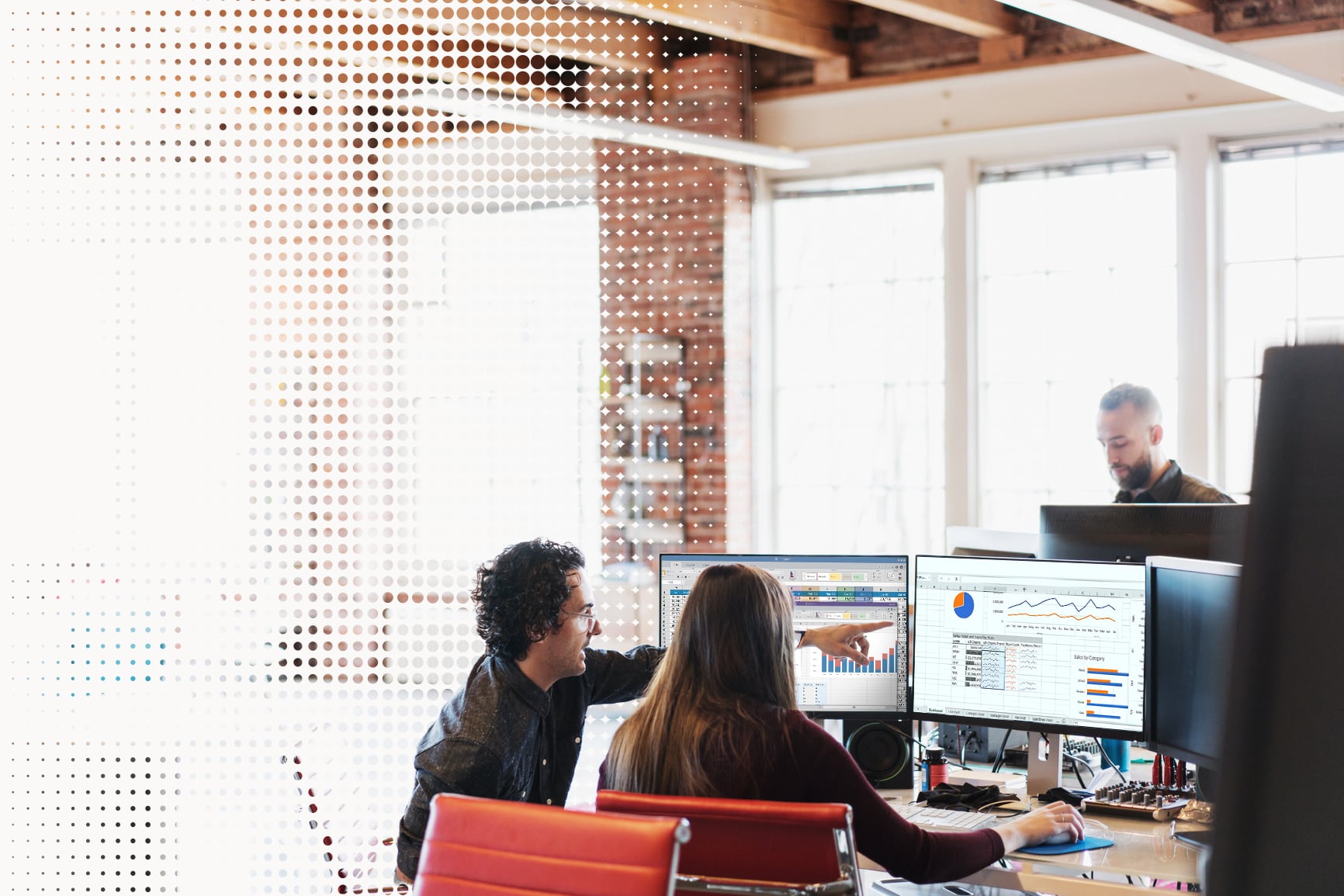 Two colleagues review spreadsheets and dashboards across dual monitors