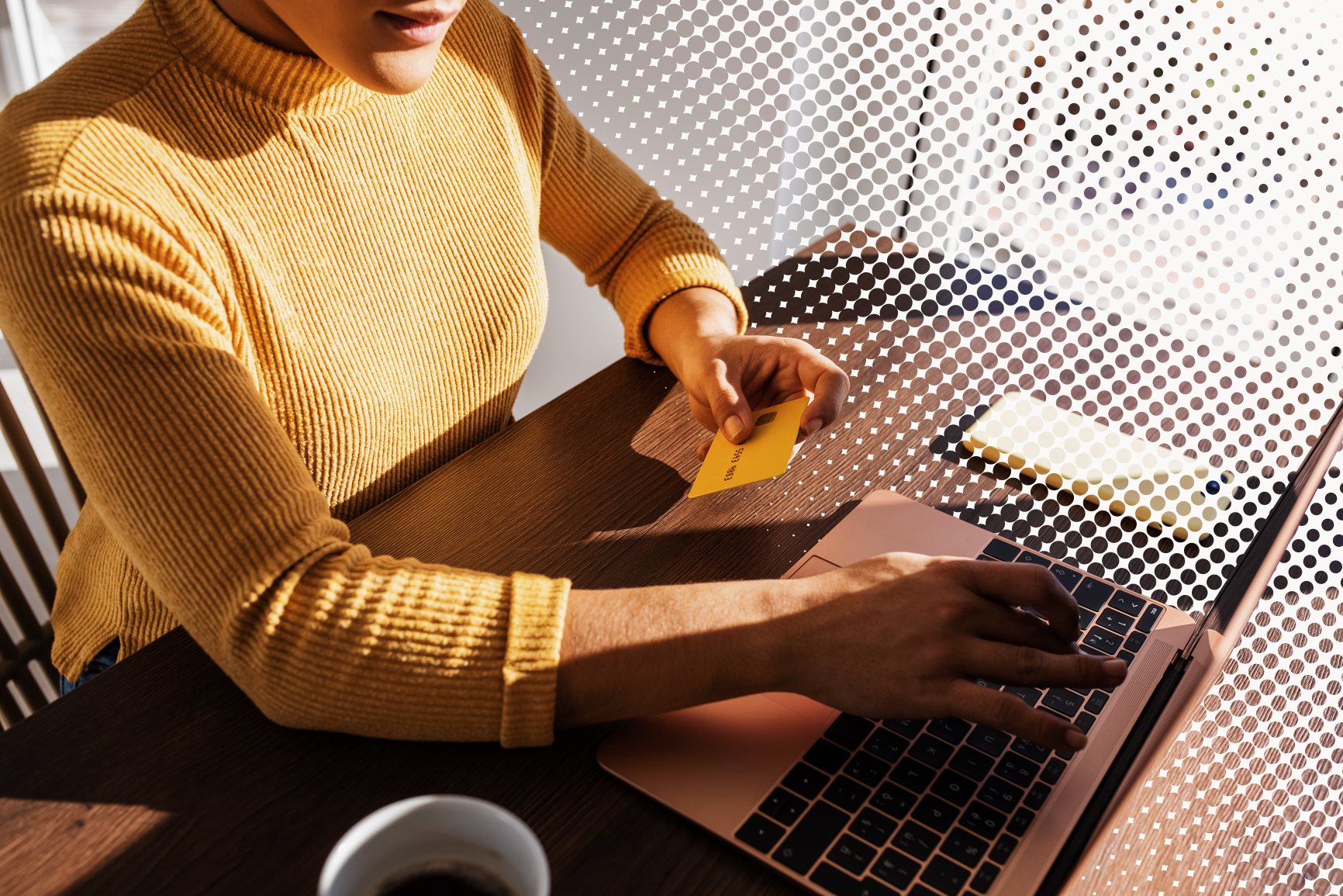 Hands hold a bank card beside a laptop keyboard in warm sunlight